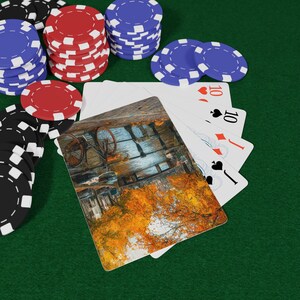 Puede incluir: Escena de juego de póquer con cartas y fichas. Las cartas muestran un diez de corazones, un diez de picas y otras cartas. Montones de fichas rojas, azules y negras están sobre una superficie de fieltro verde.