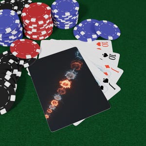 May include: Poker chips in black, red, and blue are stacked on a green felt surface. Playing cards are fanned out, with a black card featuring a colorful design. The cards show the ten of hearts, diamonds, spades, and clubs.