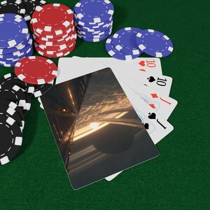 Puede incluir: Fichas de póquer negras, rojas y azules apiladas sobre una superficie de fieltro verde. Cartas de juego con el número 10 abanicadas. Una carta muestra un paisaje urbano futurista al atardecer.