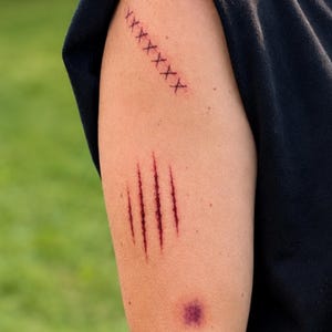 May include: A temporary tattoo set featuring a series of dark red claw marks, a row of black stitched cross marks, and a small purple bruise-like circular mark. These realistic designs are applied to the skin to simulate various injuries.
