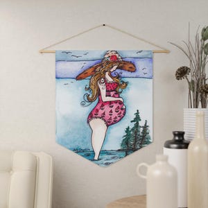 May include: A watercolour wall hanging showing a pregnant person in a pink swimsuit and a large sun hat. The artwork depicts a seaside scene with trees and birds. The artist's signature is visible.