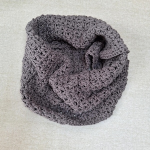 Peut inclure: Une écharpe infinie gris foncé présentant un motif en maille crochetée épaisse. L'accessoire est construit avec un design de point à boucles ouvertes cohérent qui crée une forme circulaire texturée, offrant un aspect uniforme.