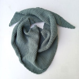May include: A sage green, hand-knitted scarf with a textured stitch pattern. The scarf is triangular, with long, pointed ends. The soft, muted colour and cosy texture suggest a handmade accessory for warmth and style.