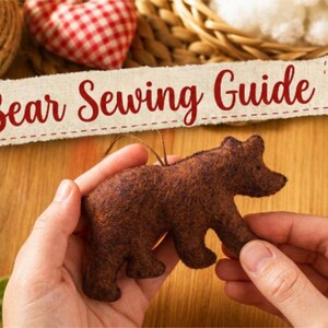 May include: A dark brown felt bear ornament with a textured surface. Above the bear, a rectangular paper label features the text Bear Sewing Guide in a red cursive font. The bear is held in place, showcasing its silhouette and small ears.