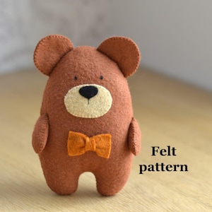 May include: A handmade brown felt bear with a cream-colored face, black nose, and orange bow tie. The bear has small ears and arms. The text "Felt pattern" is visible in the image. This item is a craft project.