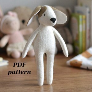 May include: A handmade white stuffed dog with brown ears and a black nose. The dog has long, thin limbs and is standing upright. The text "PDF pattern" is printed below the dog. Other stuffed animals are in the background.