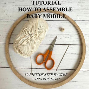Op de afbeelding: Een tutorial voor het in elkaar zetten van een babymobiel, met een houten hoepel, een bol crèmekleurig garen, een oranje schaar, een houten kraal en een naald. De tekst luidt: "TUTORIAL HOE EEN BABYMOBIELE TE MONTEREN" en "30 FOTO'S STAP VOOR STAP + INSTRUCTIES."