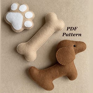 May include: A felt dog toy set including a brown dachshund, a beige bone, and a paw print with white accents. The words "PDF Pattern" are printed in black. The toys are designed for pets.