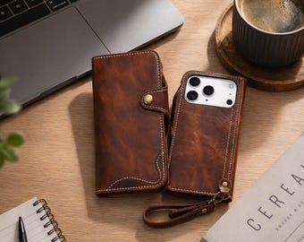 Könnte beinhalten: Zwei braune Leder-Handyhüllen, eine im Brieftaschenstil mit Knopfverschluss, die andere eine Rückseite mit Handschlaufe. Beide Hüllen haben weiße Nähte und liegen auf einer Holzoberfläche. Eine Tasse Kaffee und ein Laptop sind ebenfalls zu sehen.