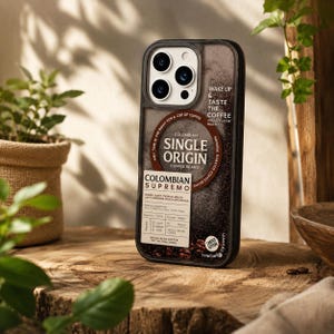 May include: A black and brown phone case with the words "Colombian Single Origin Coffee Beans." The case has a coffee bean design and the words "Wake Up & Taste The Coffee." The case is on a wooden surface.