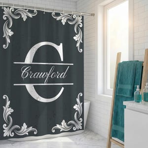 May include: A dark gray shower curtain featuring a large white letter C in the center, split by a horizontal line with the name Crawford written in white script. The curtain is decorated with white ornate scrollwork patterns in each corner.