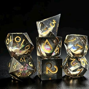 Può includere: Un set di sette dadi poliedrici trasparenti per giochi da tavolo. I dadi presentano numeri dorati e glitter iridescenti interni. Il set include un d4, d6, d8, d10, d12, d20 e un dado percentuale.