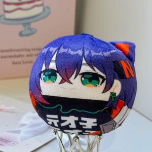 May include: A round plush toy featuring a character with short purple hair, green eyes, and a black face mask. The plush has orange accents, a small green earring, and white Japanese text printed on the lower black section of the spherical body.