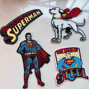May include: Embroidered patches featuring Superman and his dog, Krypto. The patches include the Superman logo, the word "SUPERMAN", and the phrase "THE MAN OF STEEL". The patches are in red, blue, yellow, and black.