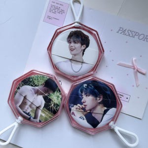 May include: Three hexagonal pink plastic keychains featuring circular photo inserts of a person. Two keychains display portraits of a person with dark hair, while the third shows a shirtless person outdoors. Each keychain has a white plastic loop.