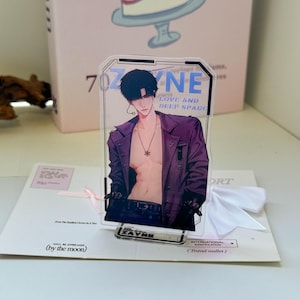 May include: A clear acrylic standee featuring an anime-style illustration of a person with dark hair wearing an open purple jacket, a necklace, and black gloves. The text ZAYNE and LOVE AND DEEP SPACE is printed in blue on the transparent surface.