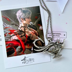 May include: A silver-toned metal pendant necklace featuring a detailed genie lamp design with a small red stone accent. The pendant hangs over a rectangular card displaying a character illustration with silver hair and red accents, plus the text 恋与深空.