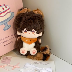 May include: A plush doll with dark brown fur, a white chest, and a bushy tail. The doll features a small orange bandana, embroidered facial features, and pink paw pads on its feet. It has rounded ears and a soft, textured appearance.