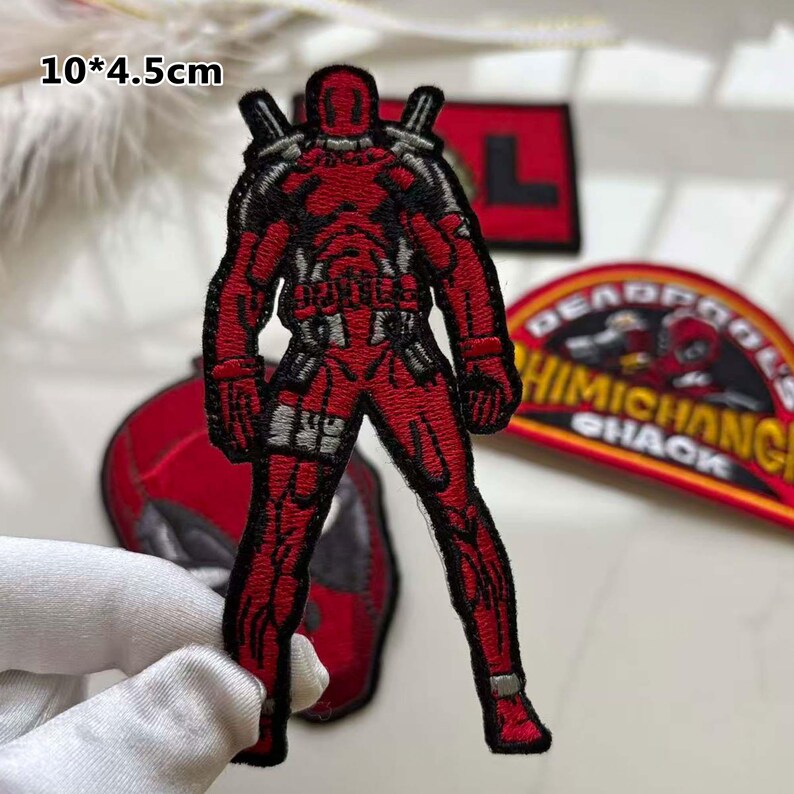May include: Embroidered red Deadpool patch, 10 x 4.5 cm, with black and grey accents. The patch features the character in a standing pose, with two katana swords on his back. Other patches are visible in the background.