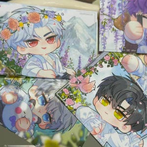May include: A collection of colorful anime-style character art cards. The cards feature illustrations of male figures with floral crowns, surrounded by flowers and birds. The color palette includes pastels and vibrant hues.