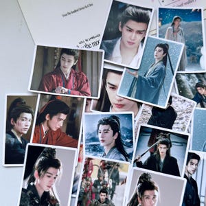 May include: A collection of rectangular stickers featuring various photographic portraits of a person with long dark hair in traditional East Asian attire, including red, blue, and black robes, set against diverse backgrounds like snowy landscapes and indoor settings.