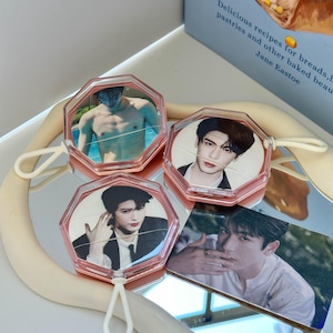 May include: Three octagonal clear plastic cases with attached white loops, each containing a circular portrait of a person. One case shows a person shirtless, another a person in a suit, and the third a person in a dark jacket. A photo card is included.