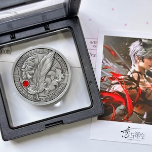 May include: A circular silver-toned metal coin featuring an embossed feather and leaf design with a small red gemstone inlay. The text "Destiny is in your own hands" is engraved along the border. The coin is displayed inside a black plastic case.