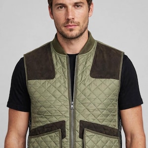 Puede incluir: Un chaleco acolchado de color verde oliva con cremallera frontal, cuello acanalado y parches de ante marrón oscuro en los hombros y bolsillos. La prenda se lleva sobre una camiseta negra y cuenta con dos bolsillos grandes.