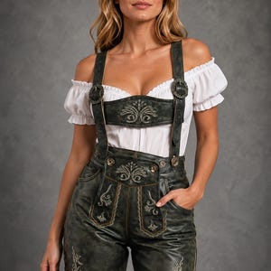 Pode incluir: Uma blusa branca de ombros caídos com mangas curtas bufantes combinada com calções de couro verde-escuro tipo lederhosen. Os calções apresentam bordados claros no peitilho e nas pernas, suspensórios ajustáveis com fivelas e atacadores.