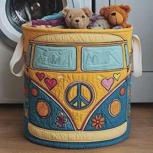 May include: A cylindrical fabric laundry hamper featuring a quilted design of a yellow and blue van with a peace sign, hearts, and flower appliqués. The hamper has two white side handles and is filled with plush teddy bears and folded textiles.