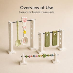 Op de afbeelding: Drie witte keramische standaards met donkere metalen staven voor het ophangen van bakprojecten. De tekst luidt Overview of Use Supports for hanging firing projects. Inclusief lepels, groene rechthoekige labels en diverse keramische kralen.