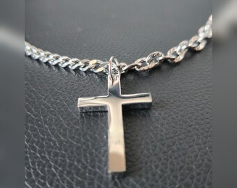 May include: A silver-toned metal cross pendant suspended from a matching curb chain necklace. The cross features a smooth, polished finish with clean, straight edges and a simple, unadorned design, attached to the chain by a small jump ring.