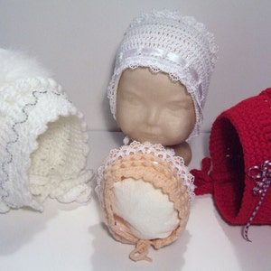 May include: Four crocheted baby bonnets in white, peach, and red. The bonnets have different lace trims and embellishments.