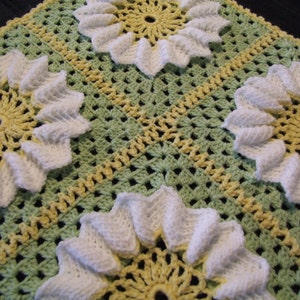 May include: A crocheted baby blanket with a green and yellow background and white crocheted flowers.