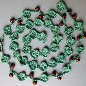 May include: A green crocheted necklace with brown wooden beads. The necklace is made of a series of connected leaf shapes.