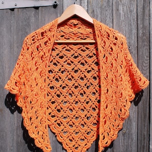 May include: A crocheted shawl in a bright orange color, hanging on a wooden hanger against a rustic wooden background.