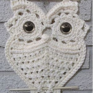 Könnte beinhalten: Weißer gehäkelter Eulen-Wandbehang mit einer kleineren grauen gehäkelten Eule, die darüber hängt. Die Eule hat unten eine Franse und ist an einem Holzstab befestigt.