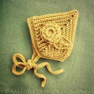 Könnte beinhalten: Eine gehäkelte Babyhaube in hellgelber Farbe mit einem Blumendesign. Die Haube hat ein Band, das unter dem Kinn gebunden werden kann.