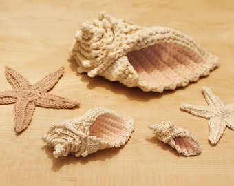 Puede incluir: Conchas y estrellas de mar de ganchillo en color beige y rosa. Las conchas son de diferentes tamaños y formas, y las estrellas de mar tienen cinco puntas.