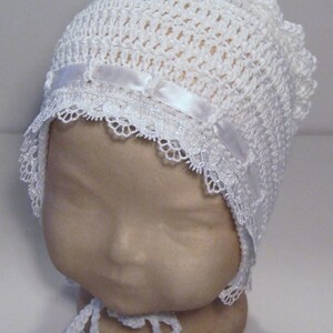 May include: White crocheted baby bonnet with a lace trim and a satin ribbon.