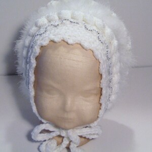 May include: White crocheted baby bonnet with a white feather trim and a silver beaded detail.