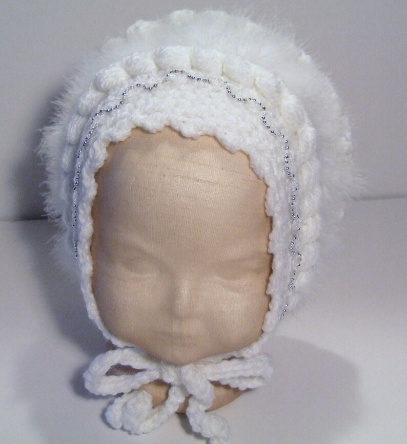 May include: White crocheted baby bonnet with a white feather trim and a silver beaded detail.