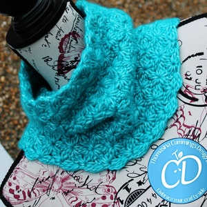 May include: A turquoise blue crocheted cowl with a flower pattern. The cowl is displayed on a white surface with black and pink floral designs and the text "Thomasina Cummings Designs" and "Embrace your crafty side".