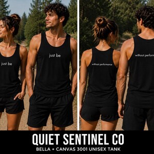 May include: A black tank top featuring the white text 'just be' on the front and 'without performance' on the back. The garment has a scoop neckline and wide shoulder straps, presented in a set showing both the front and back views of the design.