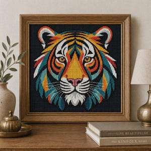 Könnte beinhalten: Gerahmtes Kreuzstich-Kunstwerk mit einem farbenfrohen Tigerkopf. Das Gesicht des Tigers ist in leuchtenden Farben wie Orange, Gelb, Blau und Weiß auf schwarzem Hintergrund dargestellt. Das Kunstwerk ist in einem Holzrahmen präsentiert, geeignet für die Inneneinrichtung.