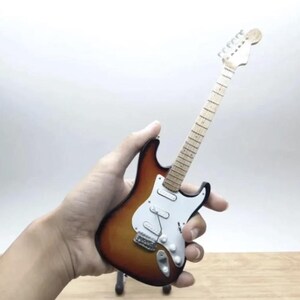 Puede incluir: Miniatura de guitarra el&eacute;ctrica con acabado sunburst, golpeador blanco y herrajes cromados. La guitarra tiene m&aacute;stil y pala de madera. El instrumento es una peque&ntilde;a r&eacute;plica de una guitarra el&eacute;ctrica de tama&ntilde;o completo.