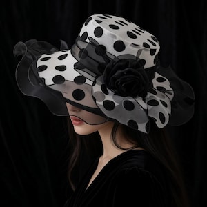 Peut inclure: Un chapeau à larges bords doté d'une base blanche à pois noirs. Le chapeau est orné d'un ruban en organza noir transparent qui entoure la calotte et comprend une grande fleur en tissu noir superposé sur le côté du bord du chapeau.