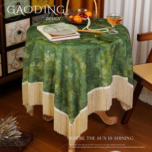 May include: A round green tablecloth with a bamboo leaf pattern and cream-colored fringe. The tablecloth is on a wooden table with a basket of fruit, a glass of liquid, and a fan. The text "GAODING DESIGN" and "WHERE THE SUN IS SHINING" are visible.