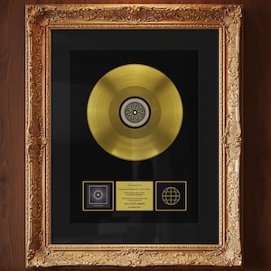 Peut inclure: Un prix de disque d'or encadré avec un cadre doré. Le disque est centré sur un fond noir, avec deux petites plaques dorées en dessous. Le cadre est orné et doré. Le prix est monté sur un panneau de bois.