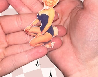 May include: A die-cut sticker featuring a blonde figure in a dark blue strapless bodysuit, white collar, and dark bunny ears. The figure is kneeling, wearing pink wrist cuffs and white high heels, with a white fluffy tail visible on the right side.